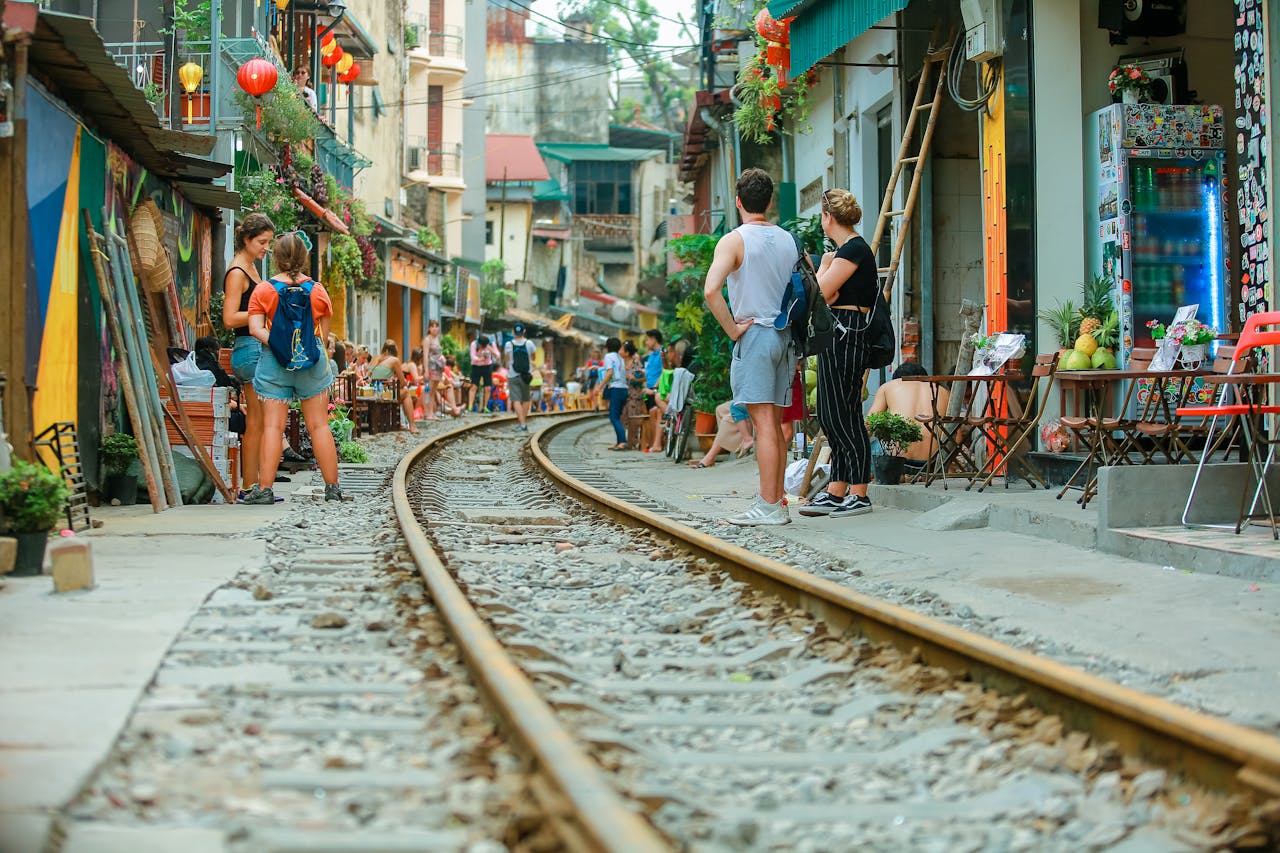 People relaxing at street cafes alongside railway tracks during daytime.